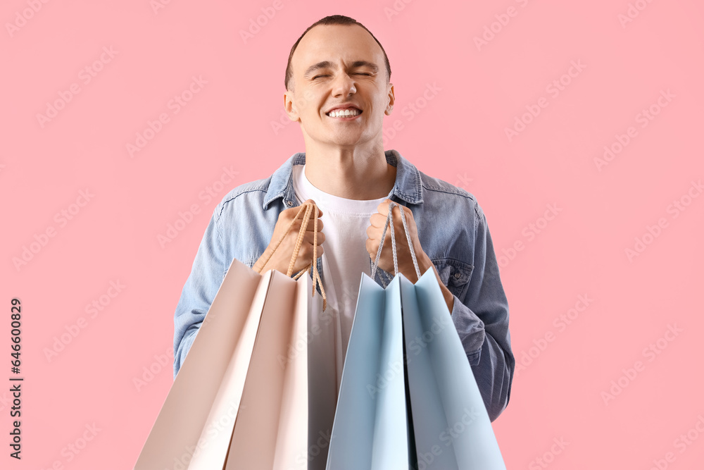 Young man with shopping bags on pink background