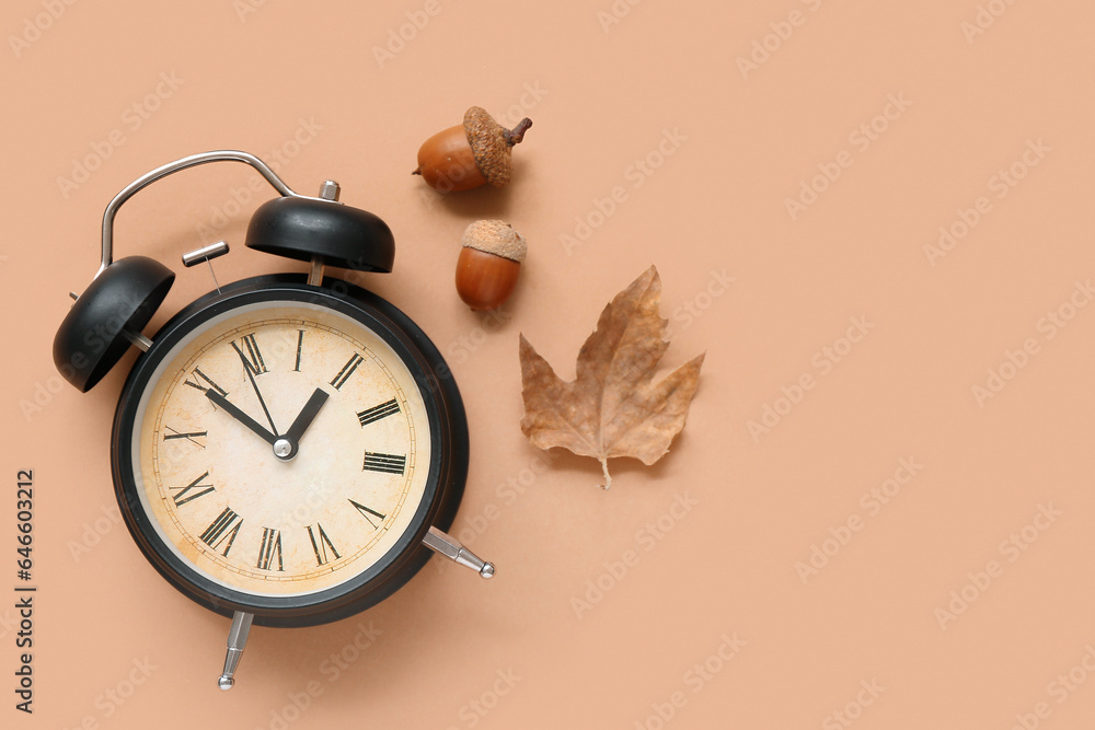 Alarm clock with fallen leaf and acorns on beige background