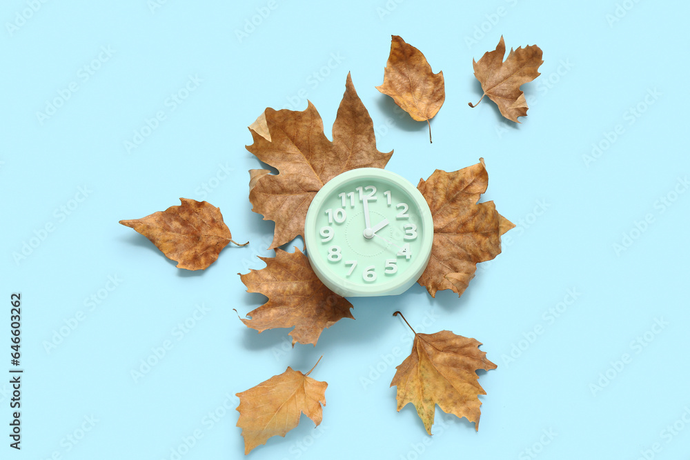 Alarm clock with fallen leaves on blue background