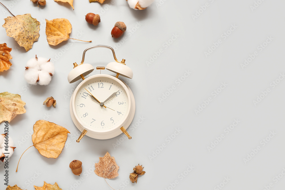 Alarm clock with fallen leaves, acorns and cotton flowers on light background