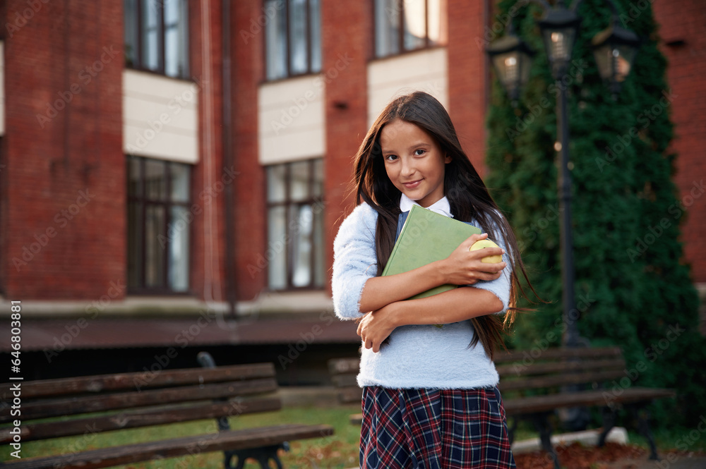 In uniform, against building. School girl is outdoors