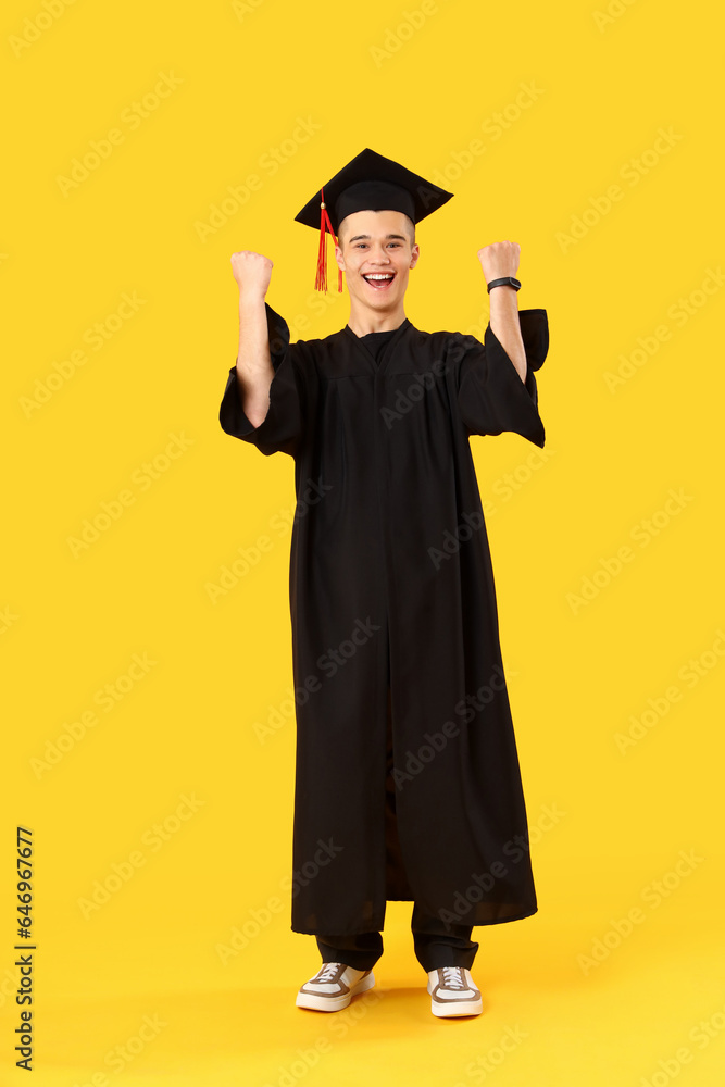 Happy male graduate student on yellow background