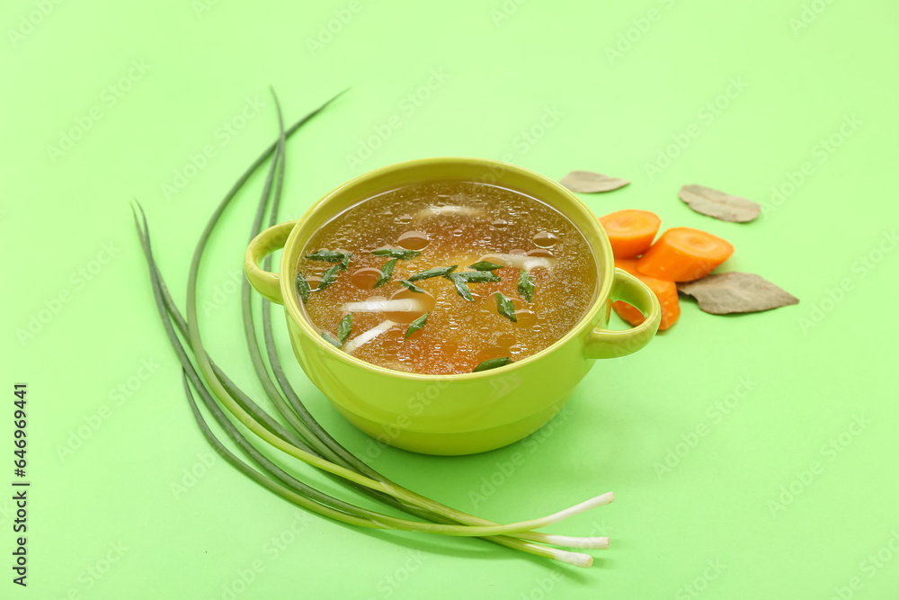 Pot of tasty vegetable broth on green background