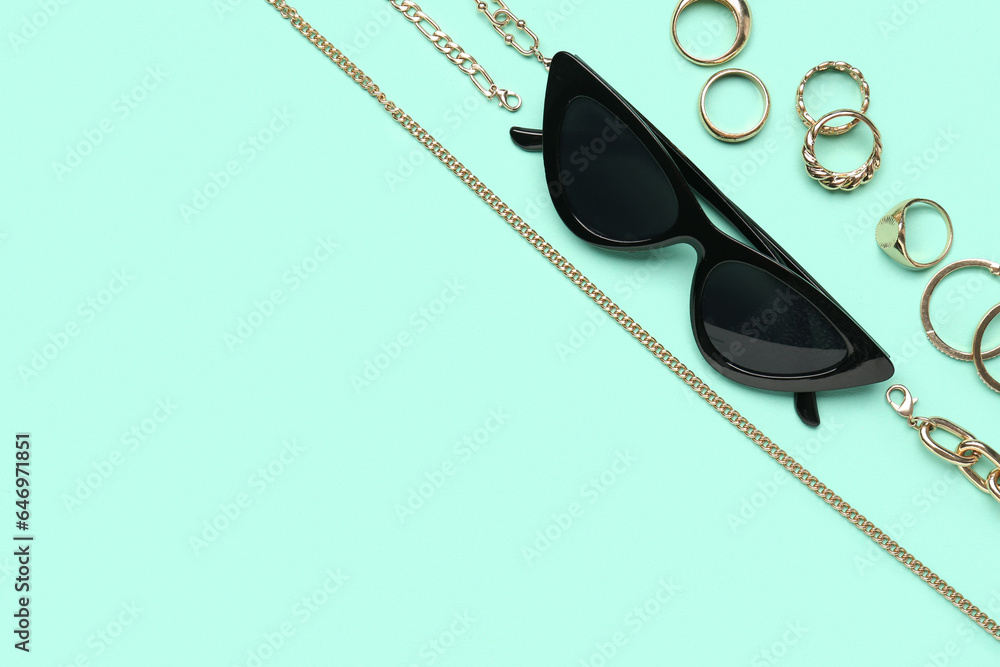 Stylish sunglasses with beautiful jewellery on turquoise background