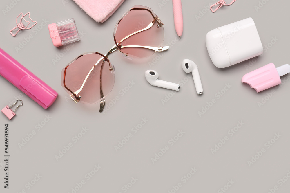 Stylish sunglasses with stationery supplies and earphones on grey background