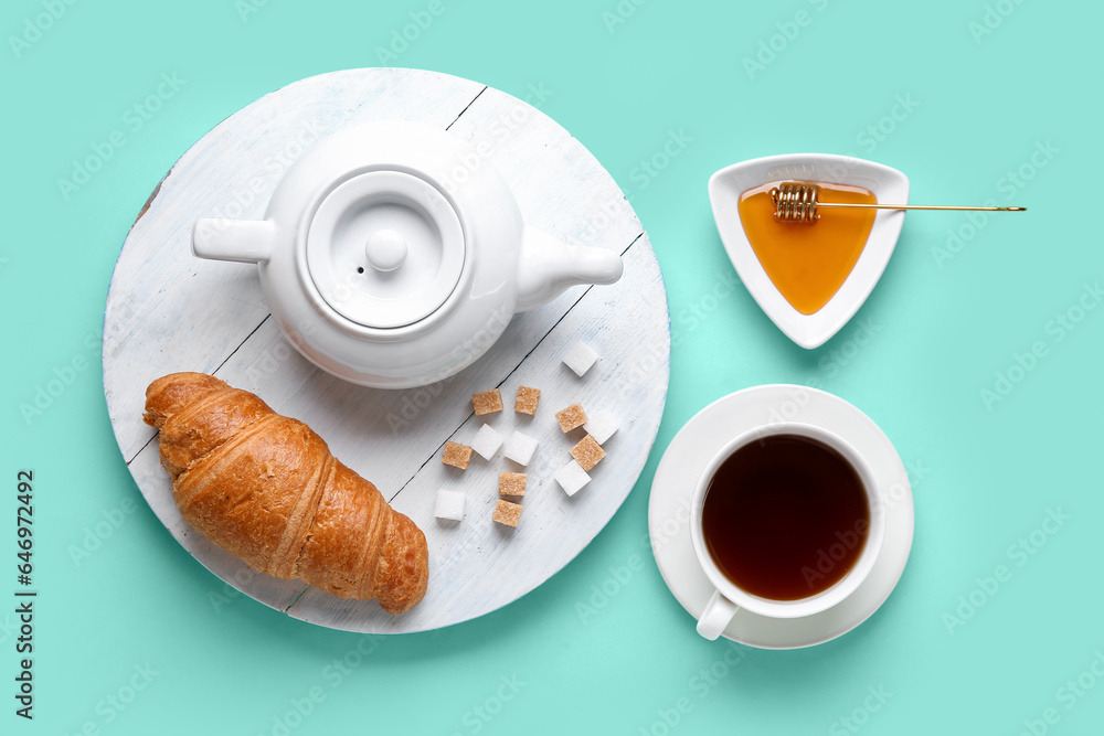 Wooden board with teapot, croissant, honey and cup of tea on color background