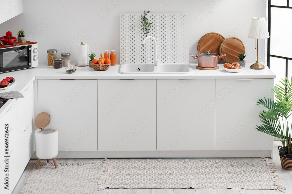 Interior of modern kitchen with stylish rug, trash bin and white counters