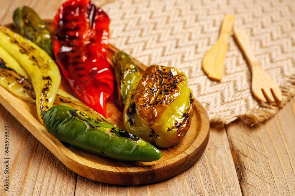 Board with different grilled peppers on wooden background