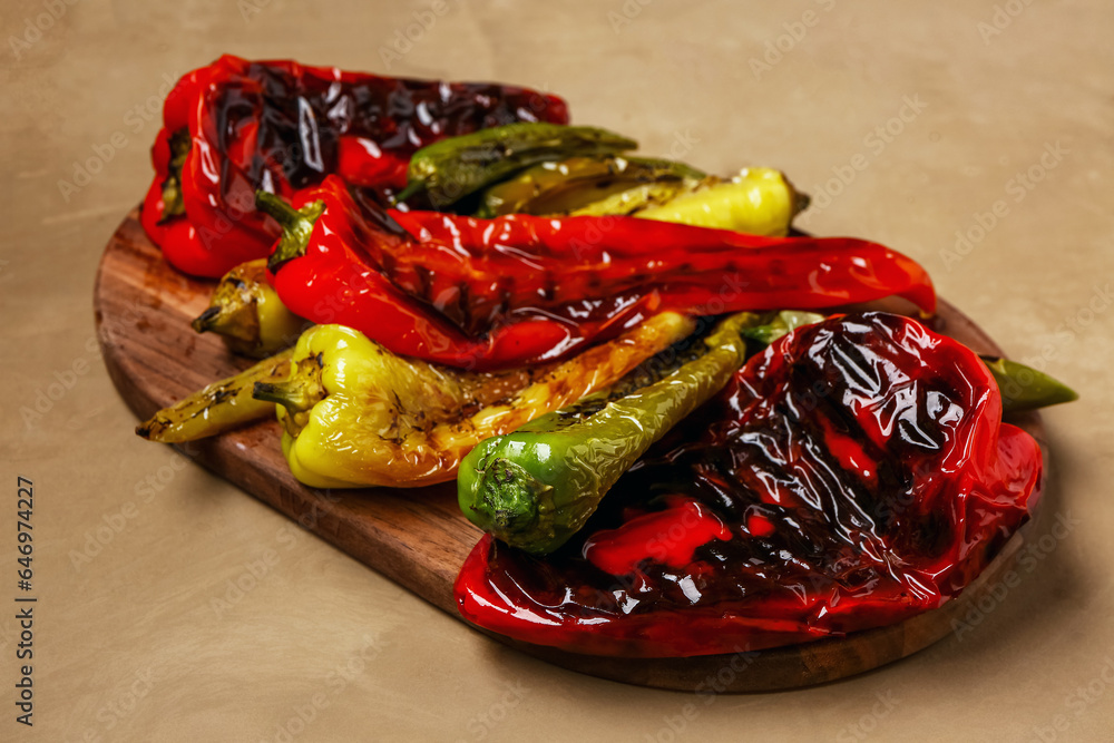 Wooden board with different grilled peppers on brown background