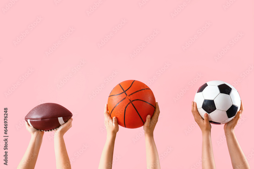 Female hands holding different sports balls on pink background