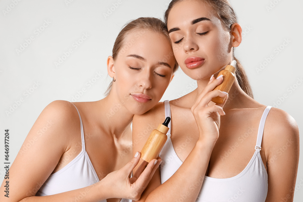 Young women with bottles of natural serum on light background