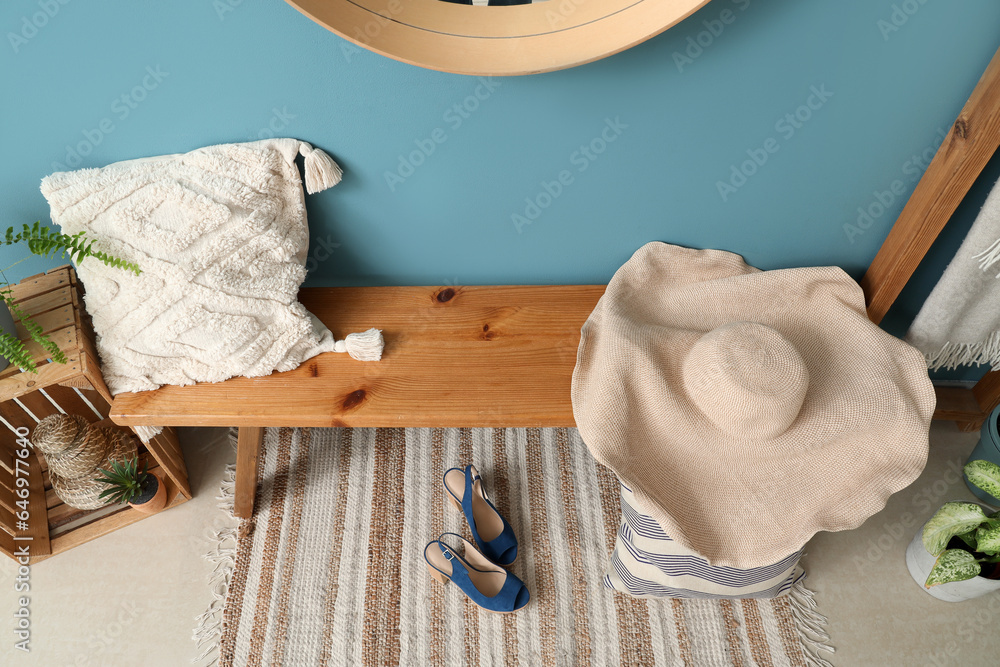 Wooden bench with pillows, female accessories and houseplants near blue wall in hall