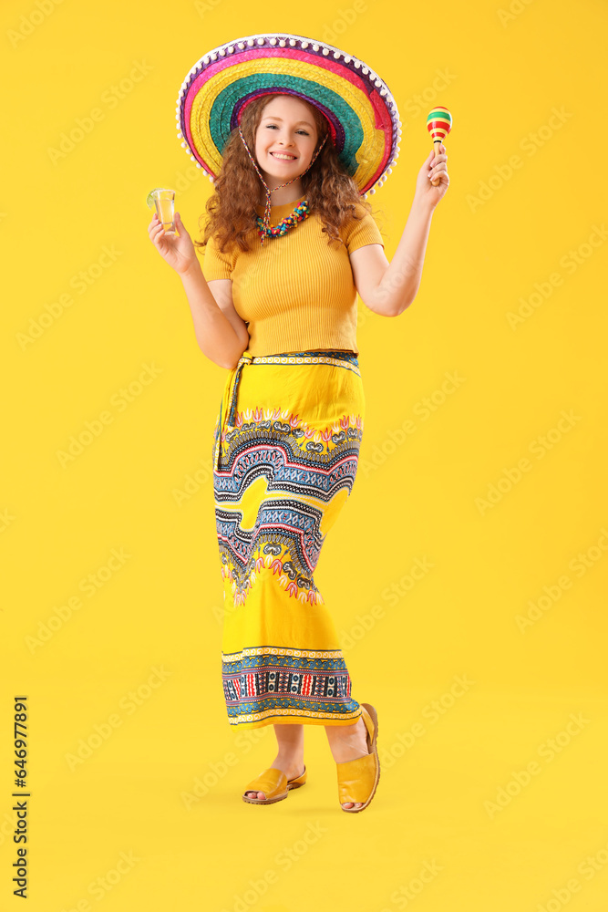 Happy Mexican woman with tequila and maracas on yellow background