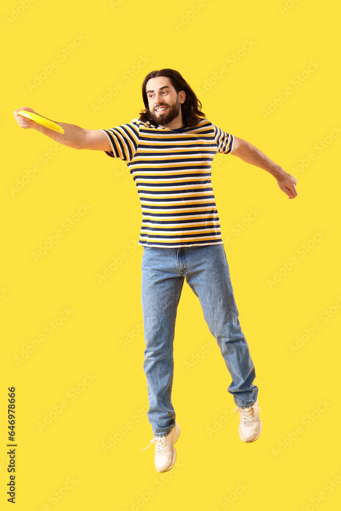 Jumping young man playing frisbee on yellow background