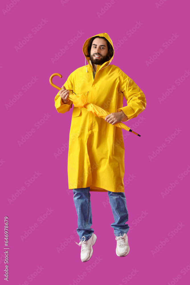 Jumping young man in raincoat and with umbrella on magenta background