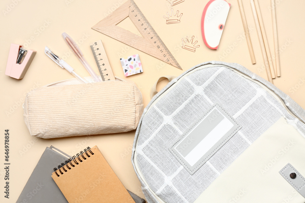 Stylish school backpack and pencil case with different stationery supplies on beige background