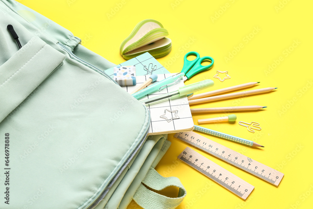 Stylish school backpack with different stationery supplies on yellow background