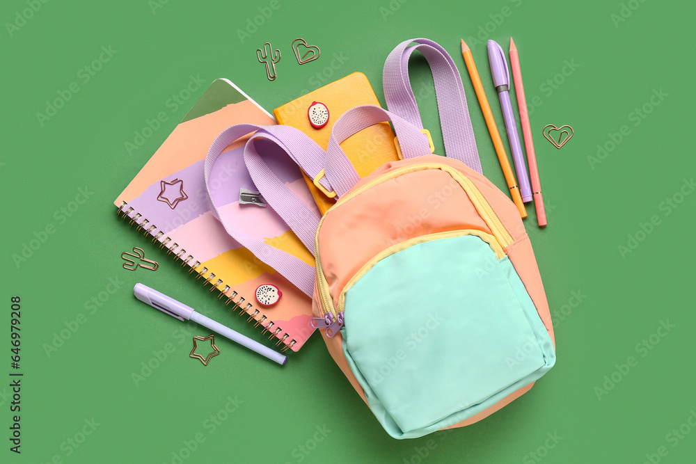 Stylish school backpack with different stationery supplies on green background