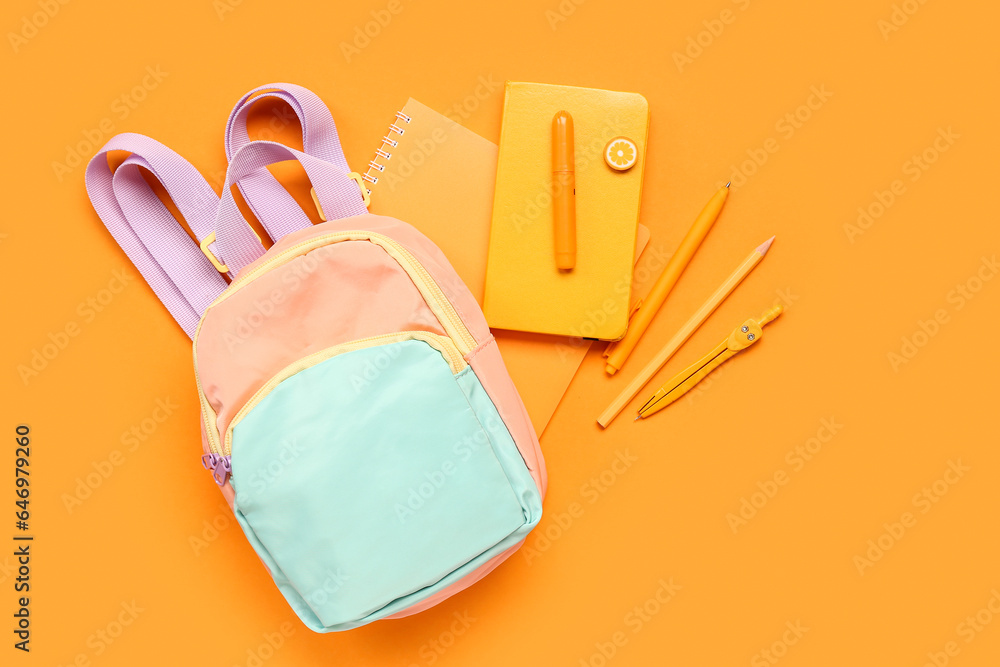 Stylish school backpack with different stationery supplies on orange background