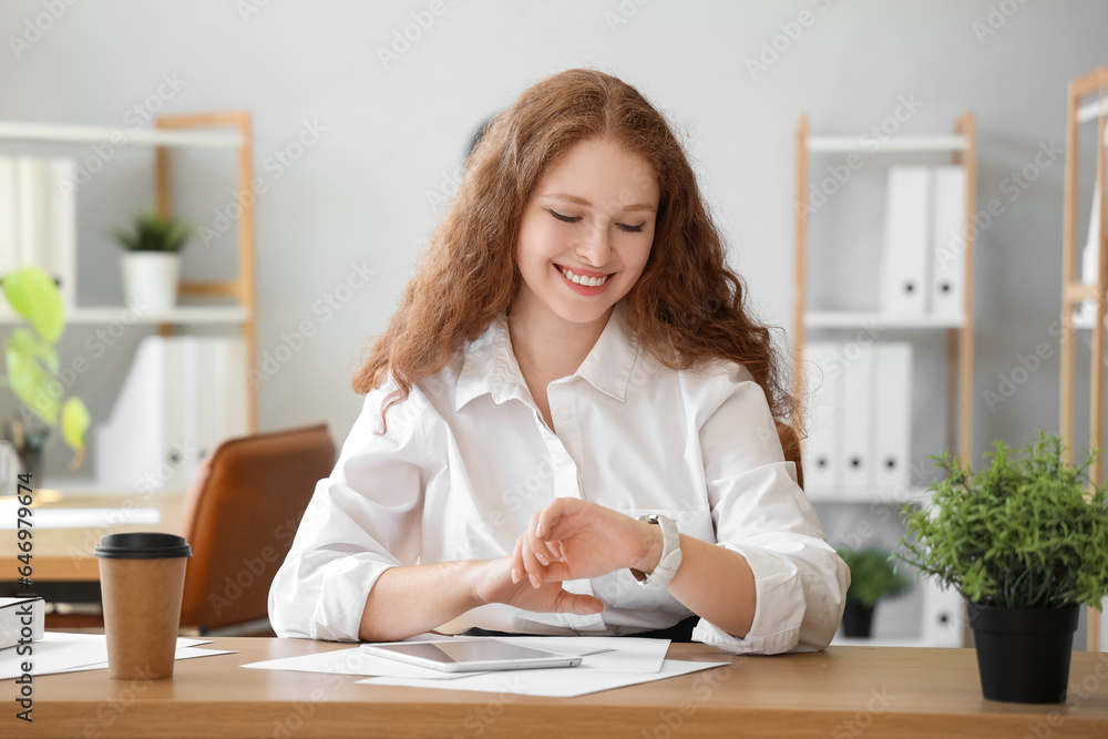 Young businesswoman looking at wristwatch in office