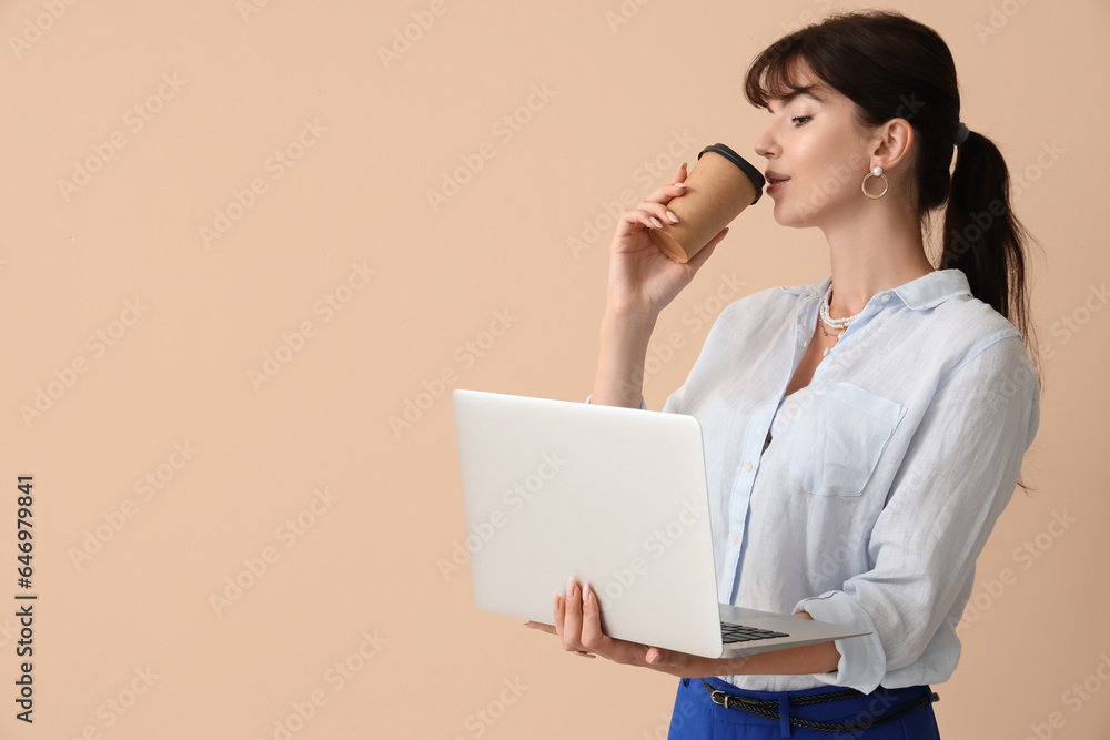 Beautiful businesswoman with laptop drinking coffee on beige background