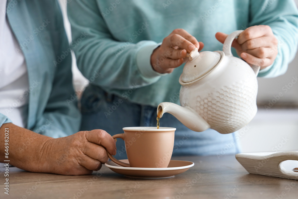 Young woman pouring hot tea for her mother in kitchen, closeup