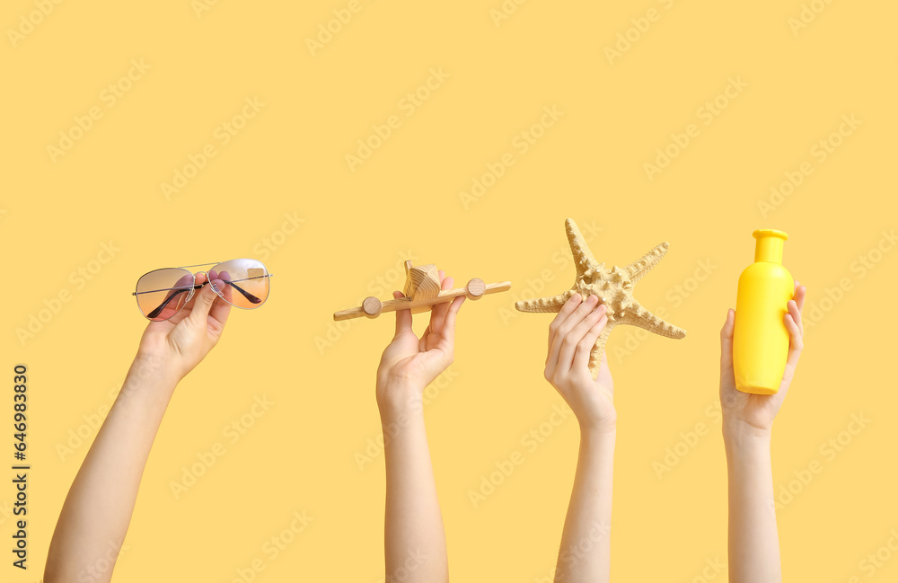 Female hands holding summer accessories on yellow background