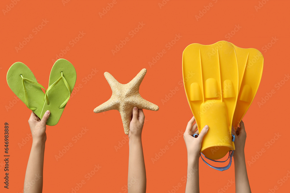 Female hands holding summer accessories on orange background