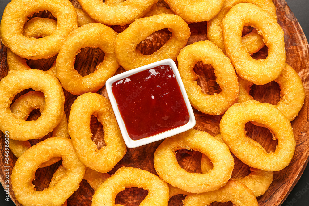 Wooden board with fried breaded onion rings and ketchup, closeup