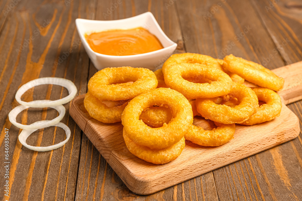 Board with fried breaded onion rings and sauce on wooden background