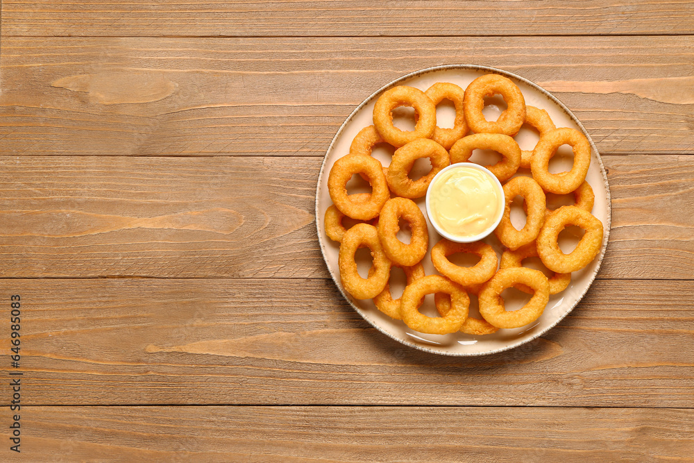 Plate with fried breaded onion rings and mayonnaise on wooden background