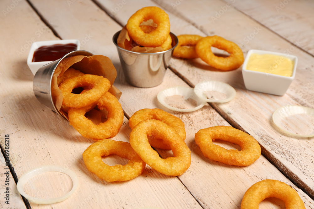 Metal buckets with fried breaded onion rings and different sauces on white wooden background