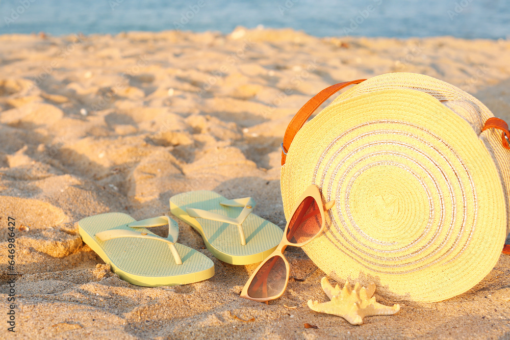 Stylish sunglasses with wicker bag, flip flops and starfish on seashore