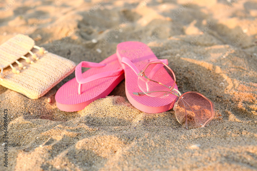 Stylish pink sunglasses with flip flops and wicker bag on sand