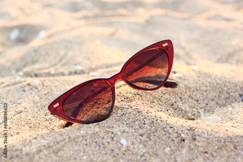 Stylish brown sunglasses on sand