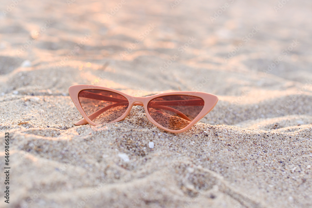 Stylish beige sunglasses on sand