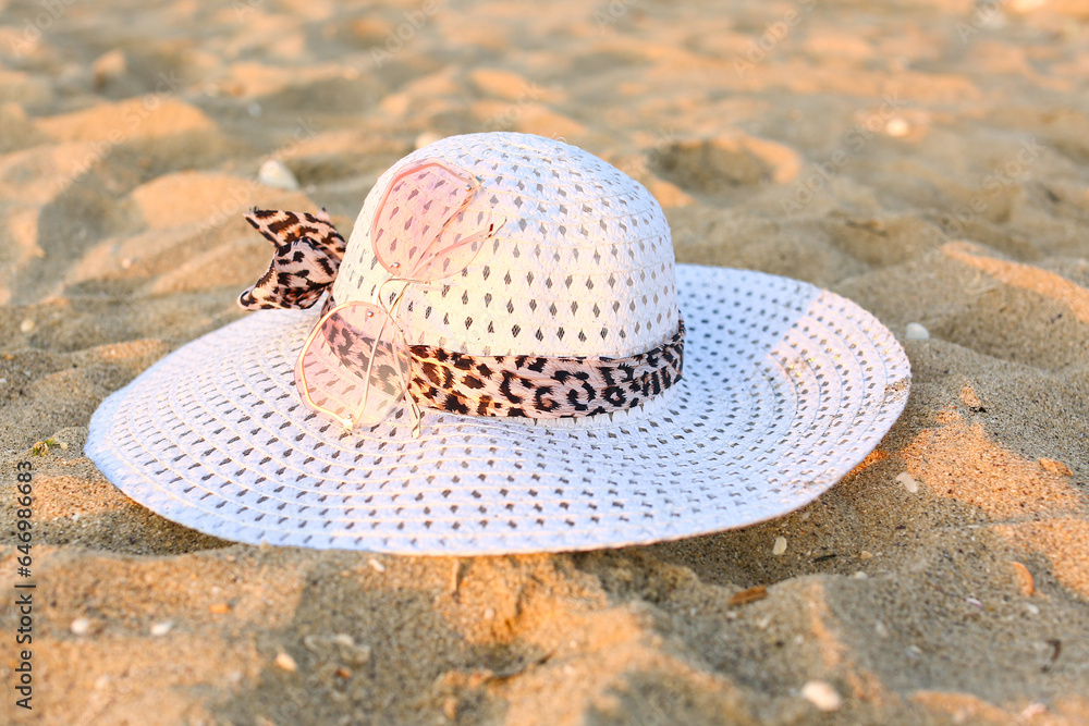 Stylish pink sunglasses and hat on sand