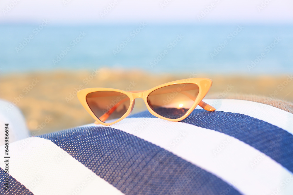 Stylish beige sunglasses on beach bag