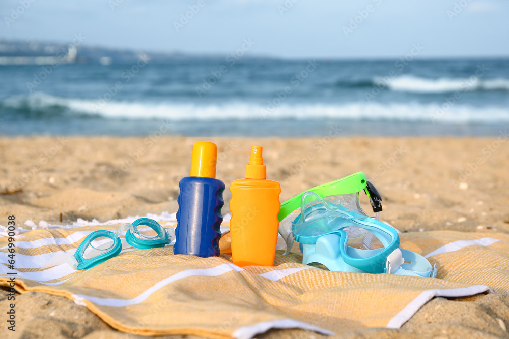 Towel with beach accessories and bottles of sunscreen cream on sand