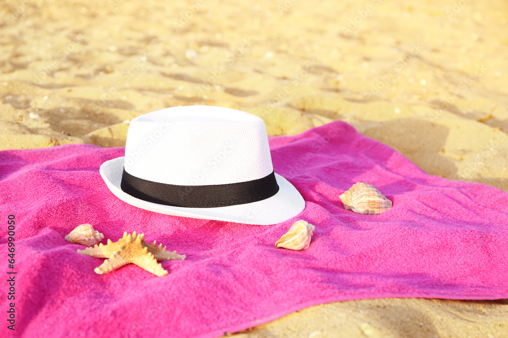 Colorful towel with stylish straw hat and seashells on sand