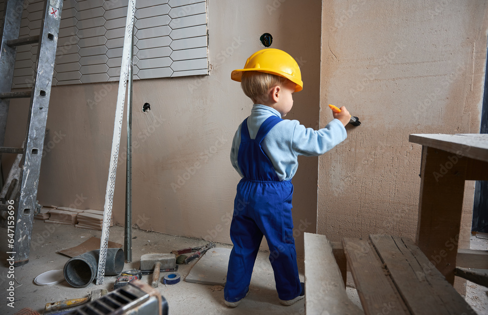 Boy construction worker painting wall with brush in apartment under renovation. Back view of child w