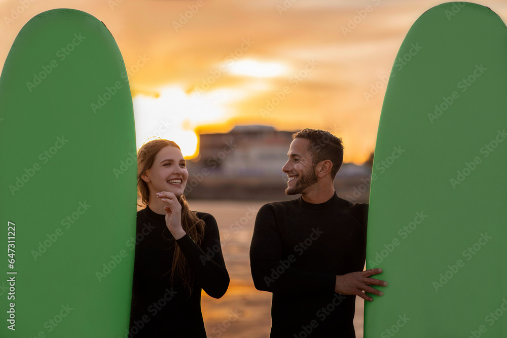 Cheerful Young Surfers Couple With Surfboards Relaxing On The Beach On Sunset