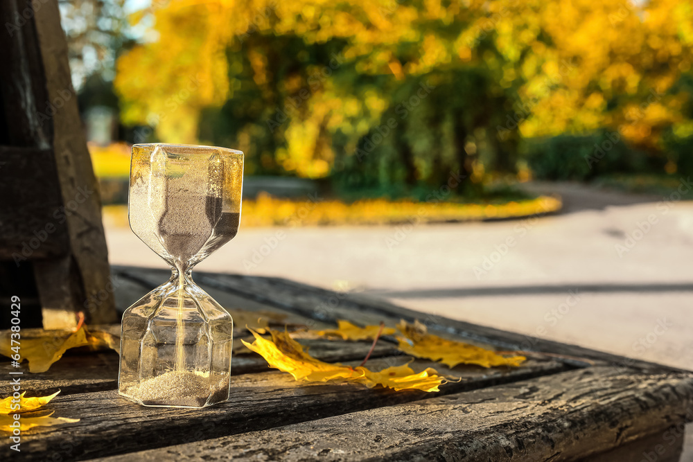 Hourglass with fallen leaves on bench in park, closeup