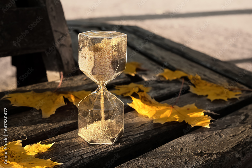 Hourglass with fallen leaves on bench in park, closeup