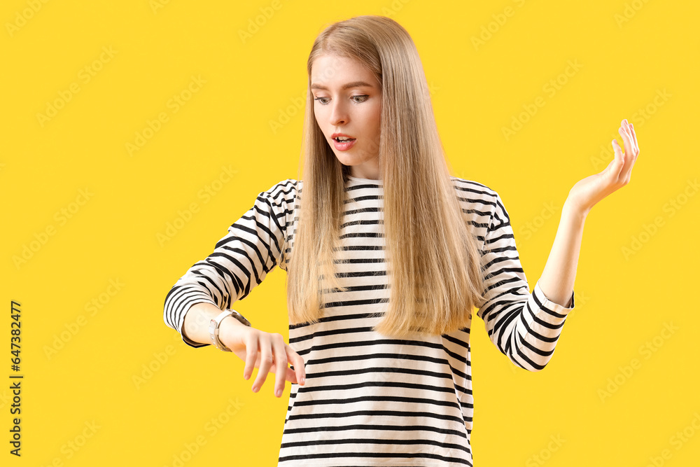 Stressed young woman looking at wristwatch on yellow background. Deadline concept