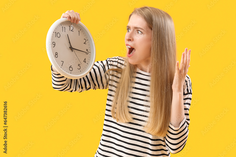 Stressed young woman with clock on yellow background. Deadline concept