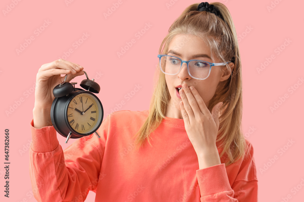 Surprised young woman with alarm clock on pink background. Deadline concept