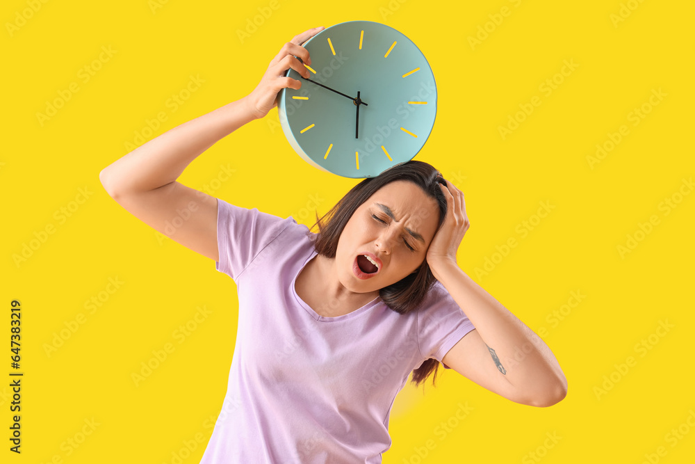 Stressed young woman with clock on yellow background. Deadline concept