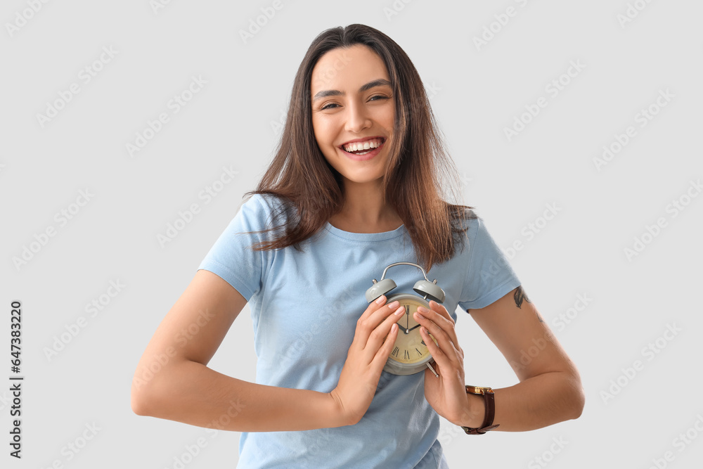 Young woman with alarm clock on light background. Deadline concept