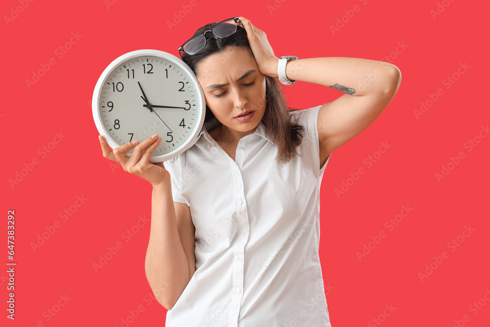 Stressed young woman with clock on red background. Deadline concept